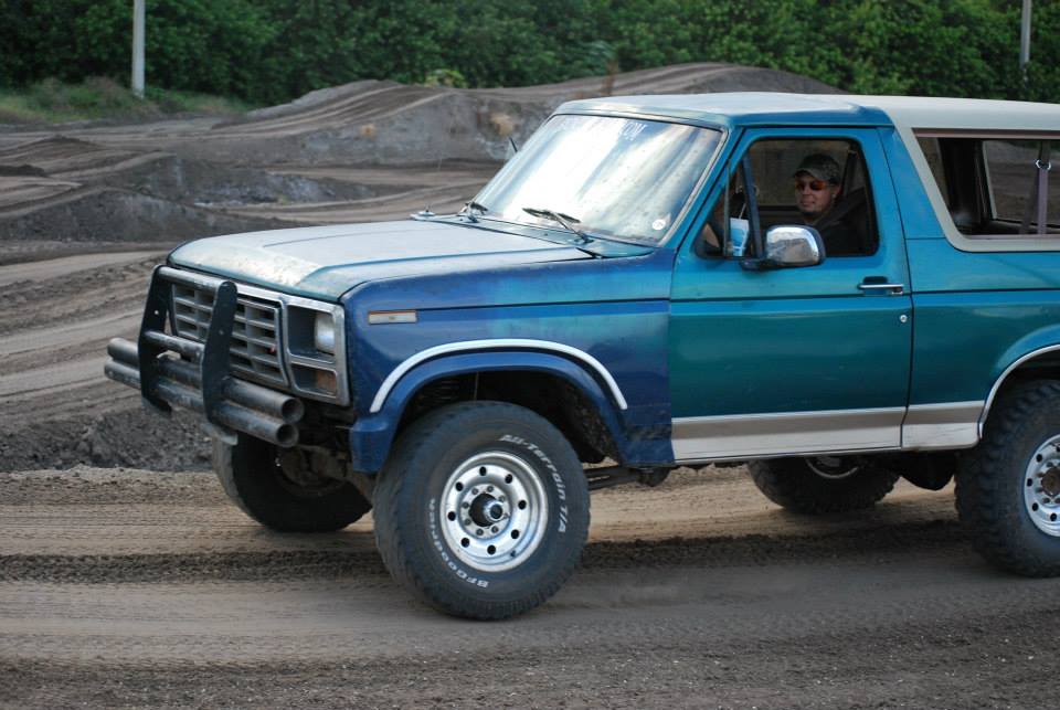 Blue Ford Bronco with a brush guard driving on a dirt track