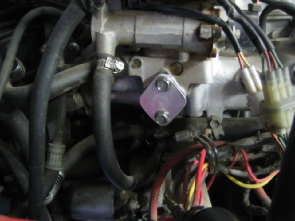 Close-up of a metal plate bolted onto an engine component, with hoses and wiring visible