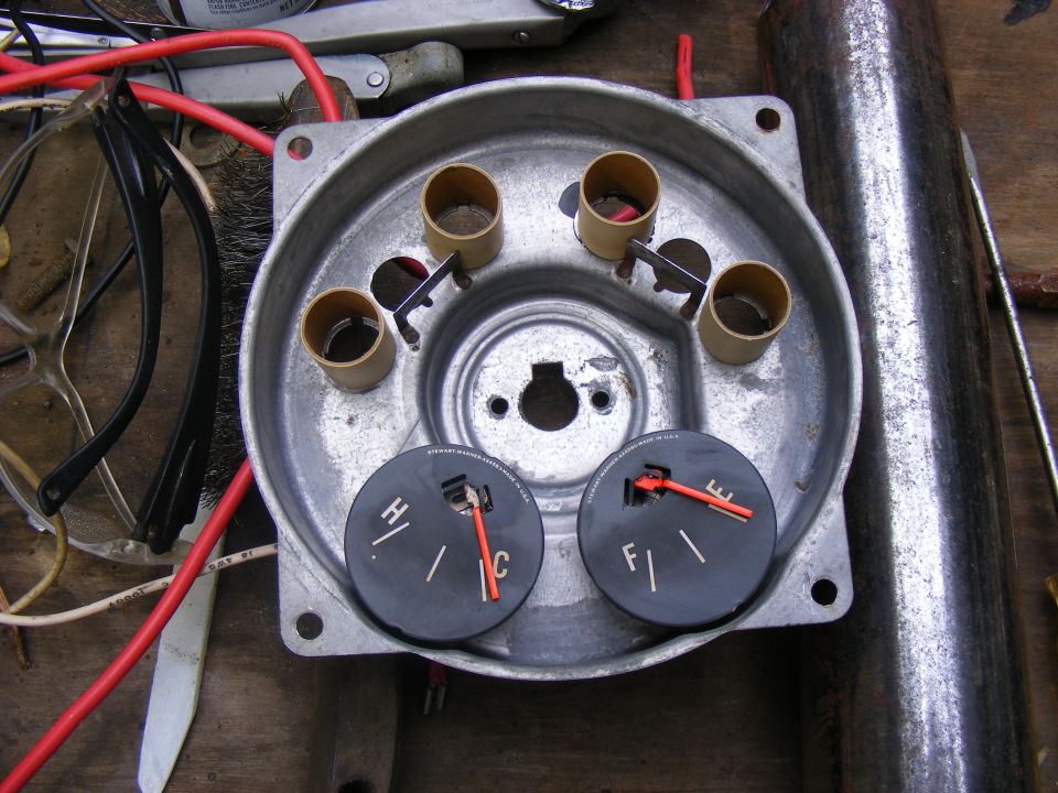 Close-up of a disassembled vehicle gauge cluster with two gauges, one for temperature and one for fuel. Wires and other parts are scattered around