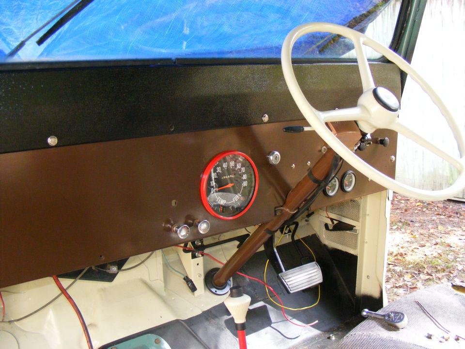 Vehicle interior dashboard with a white steering wheel, brown panel, and a red-trimmed speedometer. Wires are visible