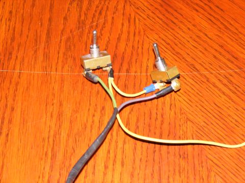 Two toggle switches with wires and a fuse connected, laid out on a wood surface
