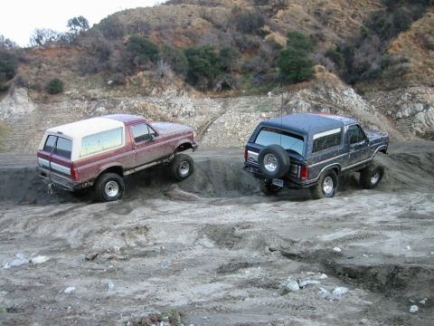 1985 Ford Bronco - Two Ford Broncos navigate a challenging dirt terrain, their off-road capabilities.