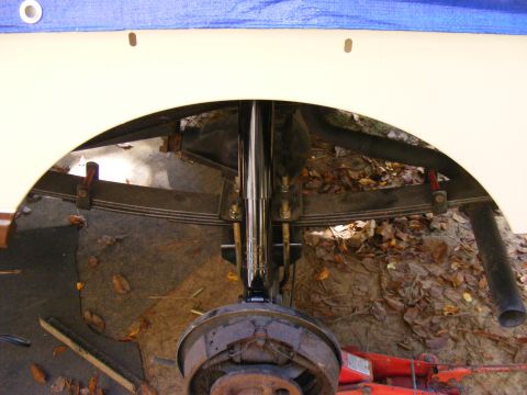 Rear axle assembly with leaf springs and brake drum, under a vehicle's wheel well