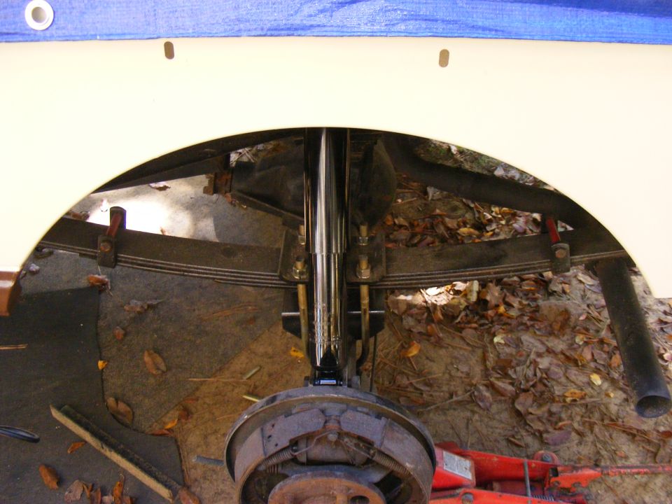 Rear axle assembly with leaf springs and brake drum, under a vehicle's wheel well
