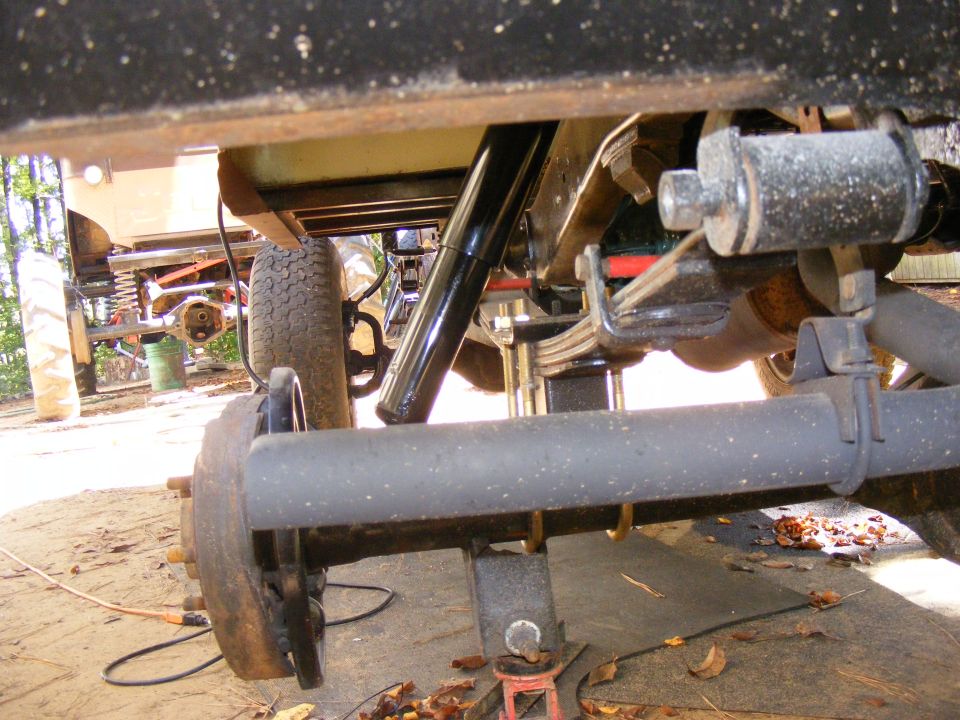 Underside view of a vehicle's rear axle, leaf springs, and shock absorber. A "SUPERMOTORS.NET" watermark is visible