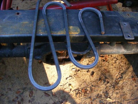 Two metal U-shaped parts resting on a rusty vehicle frame