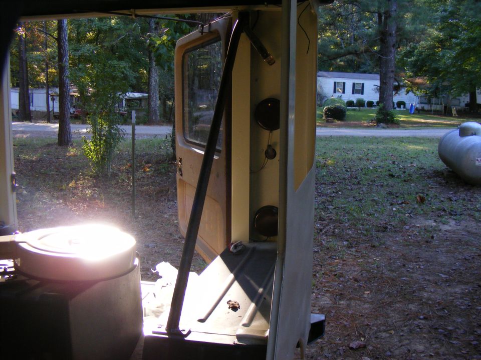 Rear of a tan vehicle with open door, showing interior components and a bright light source
