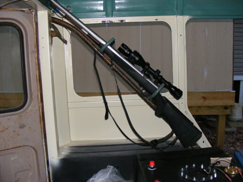 Rifle with scope mounted inside a vehicle, possibly an older SUV or truck