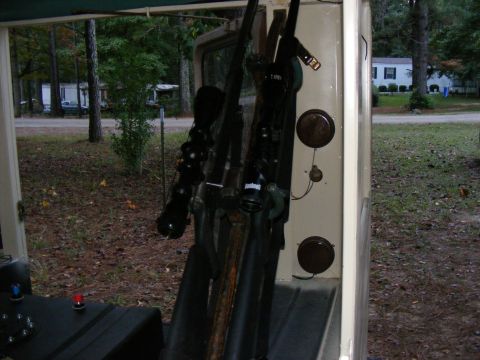 Rifles mounted on the interior wall of a vehicle, with trees and houses visible outside