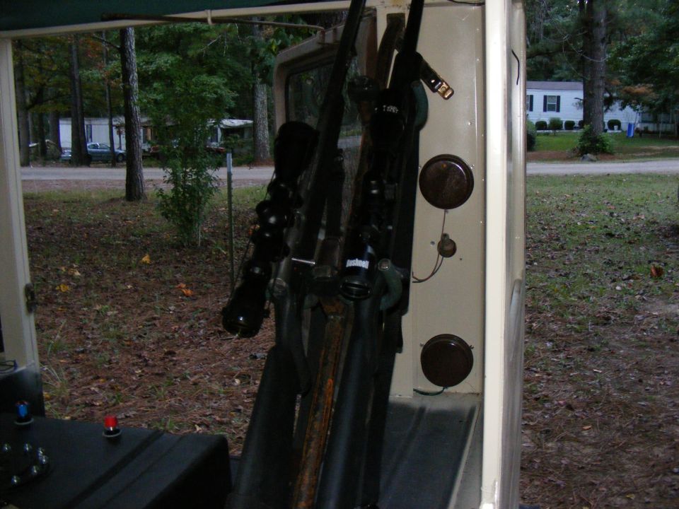Rifles mounted on the interior wall of a vehicle, with trees and houses visible outside