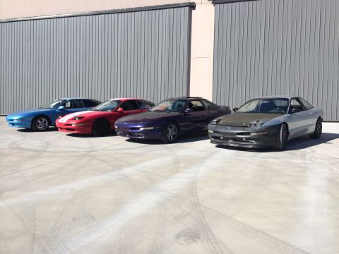 1995 Ford Probe - A collection of Ford Probes are parked in front of a large industrial building.