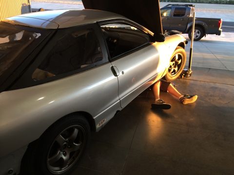1995 Ford Probe - A person works on the underside of a silver 1995 Ford Probe coupe, with a pickup truck visible in the background.