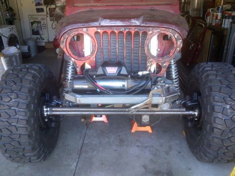 1985 Jeep CJ7 - Front view of a red Jeep CJ-series undergoing modification, a winch and oversized tires.