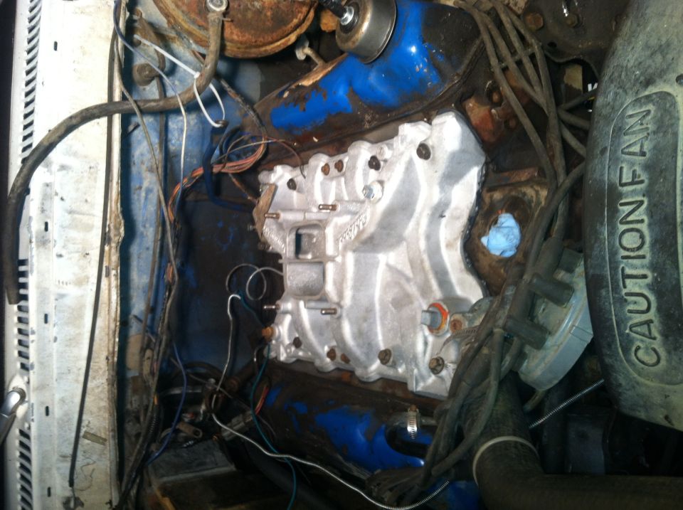 Engine bay with a silver intake manifold and blue painted valve covers. Wires and hoses are visible