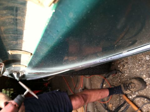 1978 Ford Bronco - A person works on the bottom edge of a green car door, with a tire visible below.