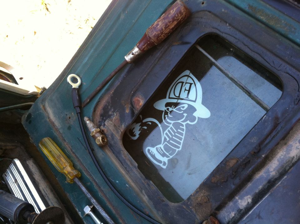 Green vehicle interior with a screwdriver, spark plug, and a sticker of a cartoon firefighter on the window