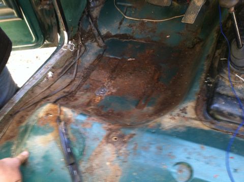 1978 Ford Bronco - The interior floor of a vehicle shows significant rust and damage, with exposed wiring and pedals visible.