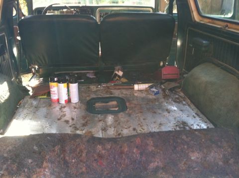 1978 Ford Bronco - The interior of a 1978 Ford Bronco shows a rusty floor and two rows of dark seats, with spray paint cans on the floor.