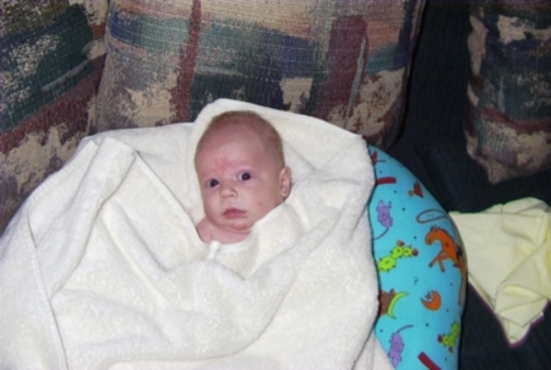 Baby wrapped in a white towel, with a patterned pillow beside