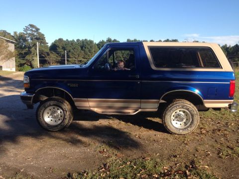 1996 Ford Bronco - Side profile of a blue 1996 Ford Bronco parked outdoors with a child visible in the driver's seat.