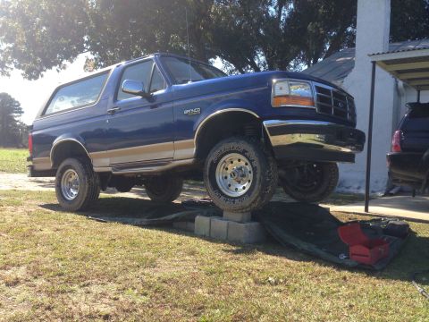 1996 Ford Bronco - A blue Ford Bronco is parked on concrete blocks in a grassy yard, with a toolbox on the ground.