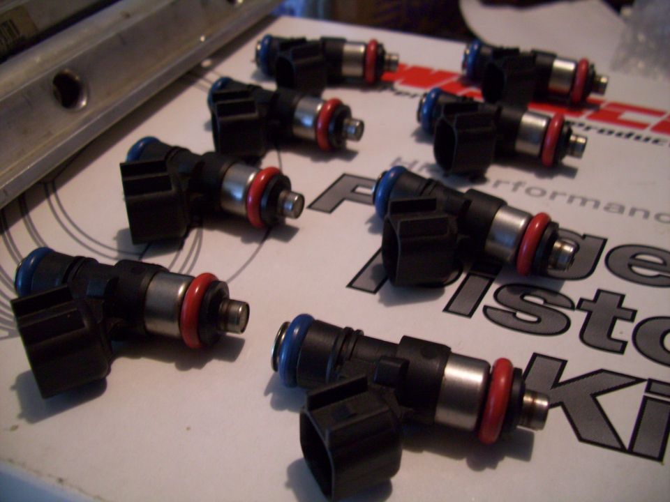 Several black fuel injectors with red and blue O-rings on a white surface with text
