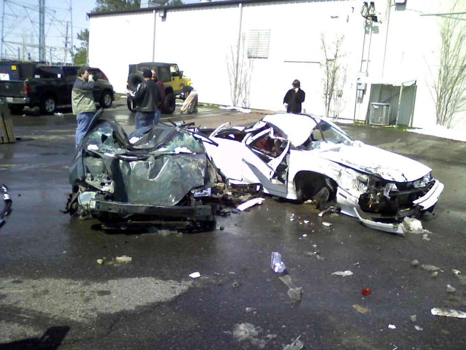 Two heavily damaged cars, one white and one green, in a lot