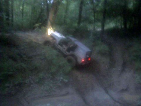 1978 Ford Bronco driving off-road, light-colored, with headlights and taillights on