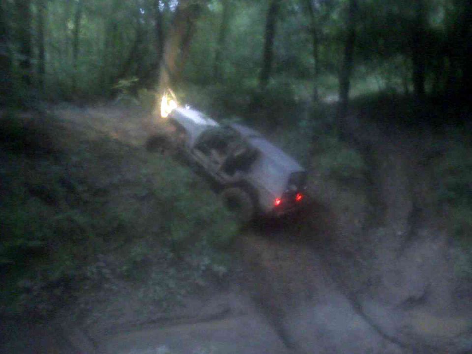 1978 Ford Bronco driving off-road, light-colored, with headlights and taillights on