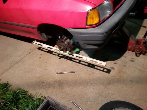1991 Ford Festiva - A red 1991 Ford Festiva's front brake assembly is exposed as the wheel has been removed and a level is placed underneath.