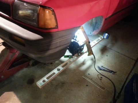 1991 Ford Festiva - A red car's front fender and bumper are visible, with a level and tools nearby, suggesting repair work.