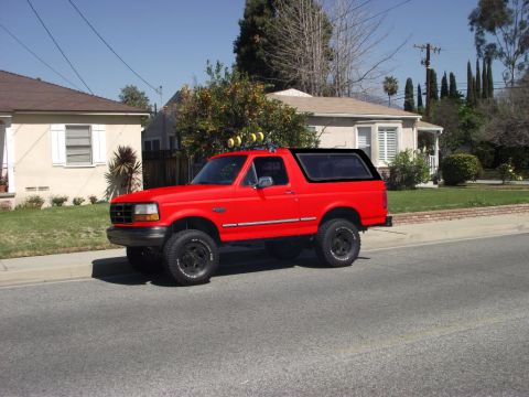 1994 Ford Bronco - This red 1994 Ford Bronco is parked on the side of a street in front of houses.