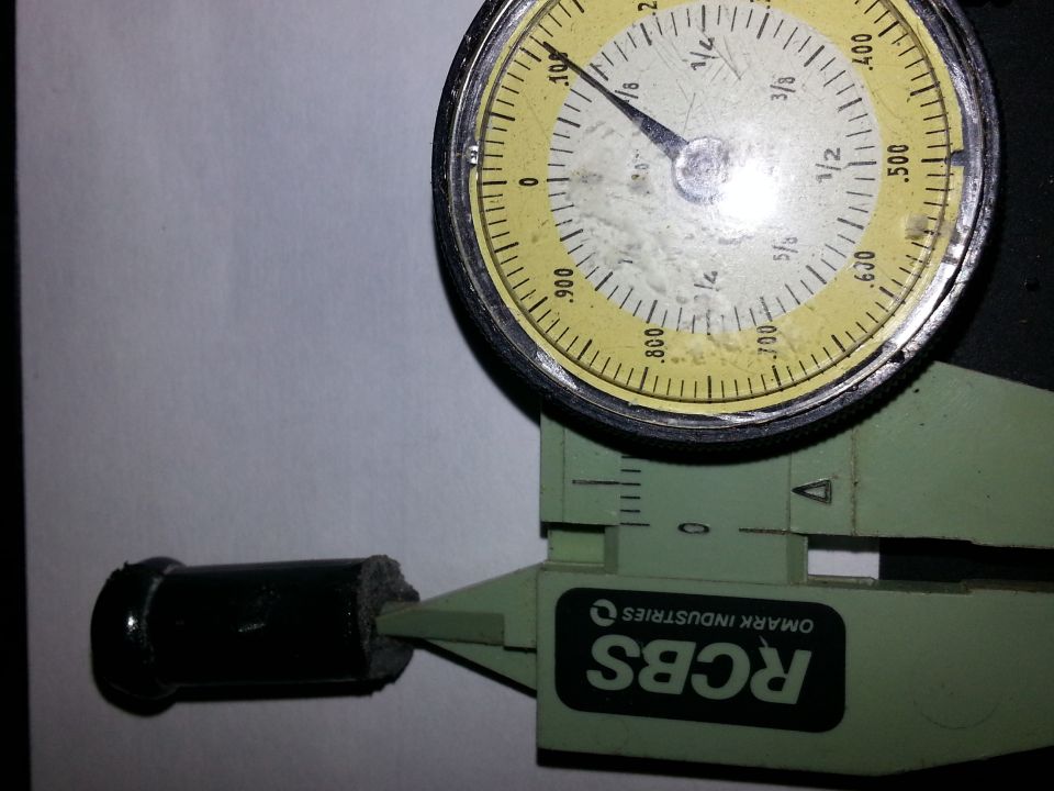 Dial caliper measuring a black cylindrical part with a rough end. Text on caliper reads 'RCBS OMARK INDUSTRIES'