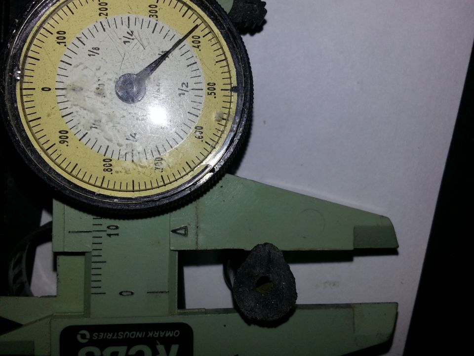 Dial indicator and caliper measuring a small, dark, circular part with a hole in the center