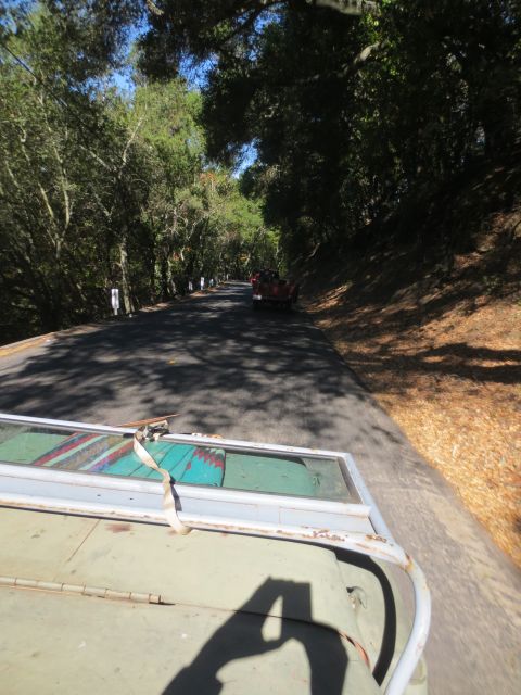 1946 Jeep CJ5 - A red convertible is seen driving on a road lined with trees, with a door being transported in the foreground.