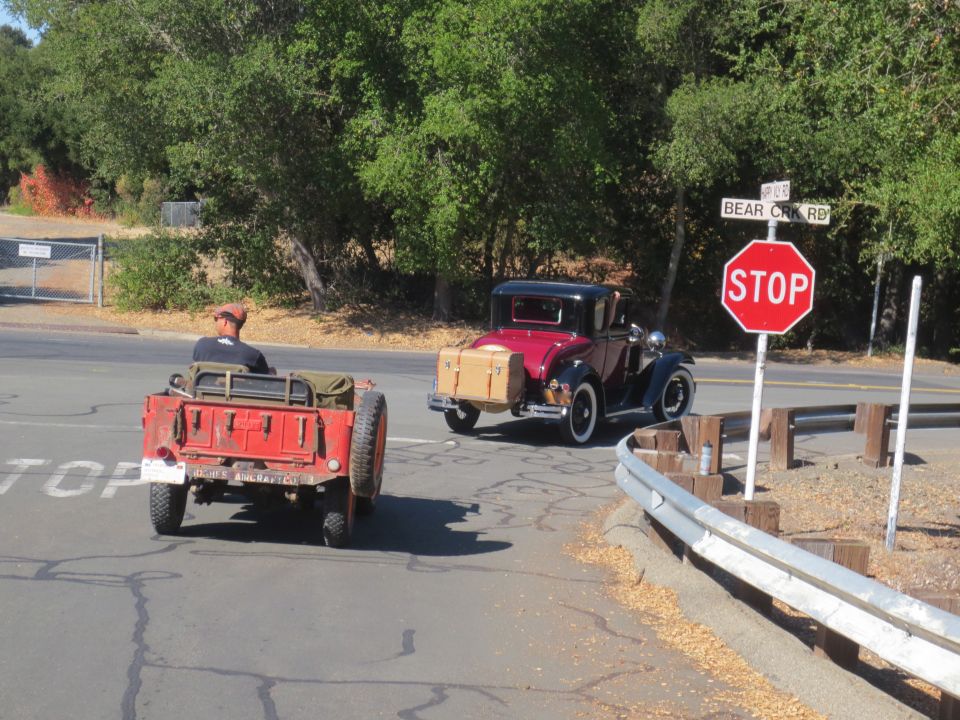 Red jeep-like vehicle with a trailer, seen from the rear, with a maroon coupe behind it