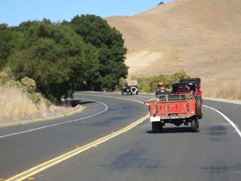 1946 Jeep CJ5 - A red 1946 Jeep CJ5 leads a vintage car procession on a sunny day.