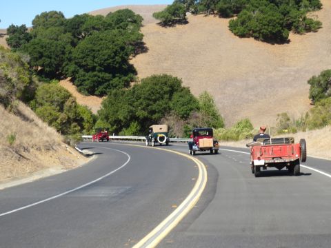 1946 Jeep CJ5 - A convoy of antique automobiles navigates a scenic route through rolling hills.