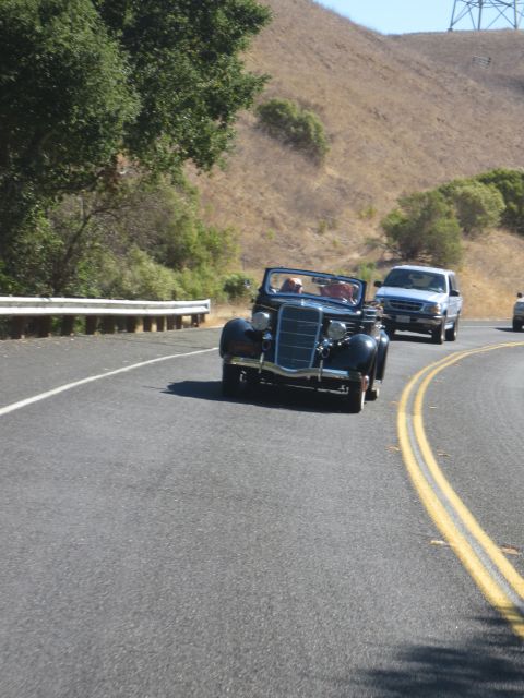 1946 Jeep CJ5 - A vintage convertible cruises down a two-lane highway on a sunny day, followed by a modern pickup truck.