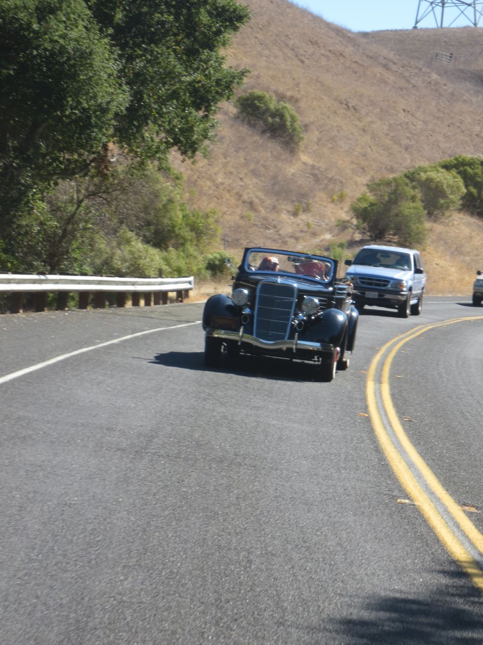 dark blue convertible driving on a road with a white pickup truck behind it