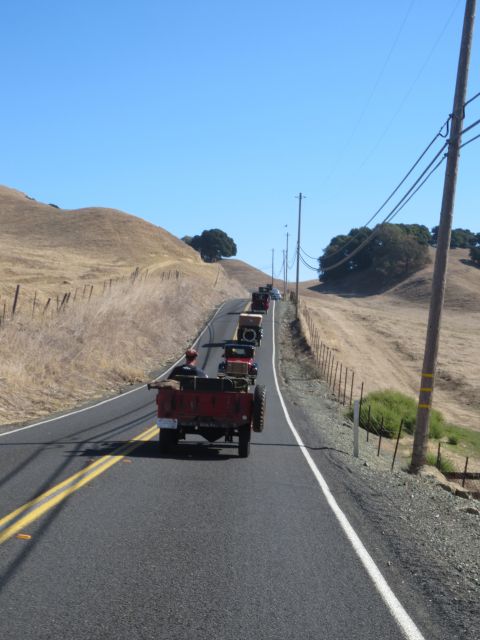 1946 Jeep CJ5 - A procession of antique vehicles travels along a winding road through a dry, hilly landscape under a clear blue sky.