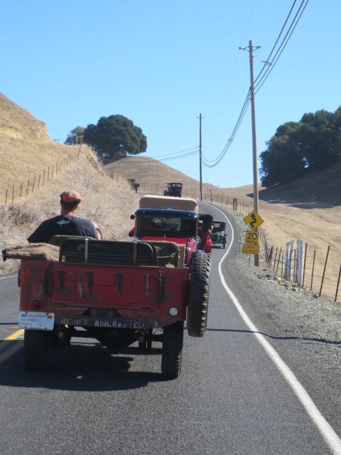 1946 Jeep CJ5 - A convoy of vintage vehicles, including a red military-style truck, travels along a winding country road under a clear blue sky.