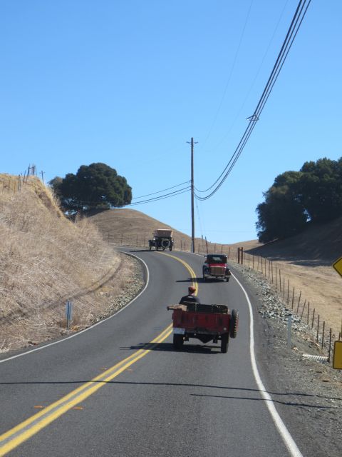 1946 Jeep CJ5 - A convoy of vintage vehicles travels along a winding rural highway under a clear blue sky.