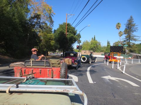 1946 Jeep CJ5 - A convoy of vintage vehicles, including a red jeep, drives down a road on a sunny day.