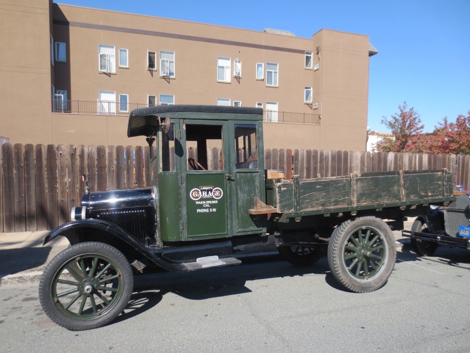 old green flatbed truck with wooden bed, black hood, and spoked wheels