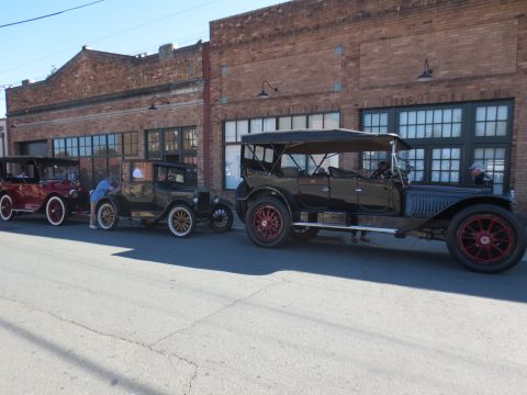 1946 Jeep CJ5 - Several vintage automobiles are lined up on a street in front of a brick building with large windows.