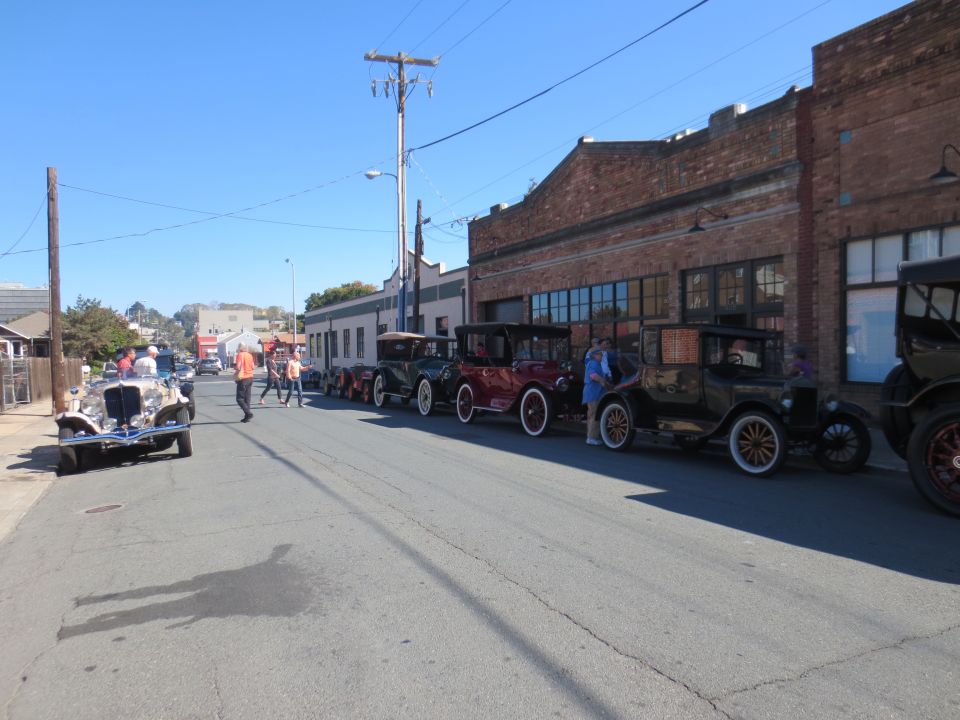 Several antique cars parked in a row on a street, with people walking around them