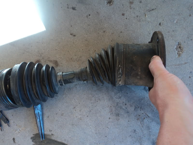 CV axle shaft with rubber boots on a concrete surface, held by a hand