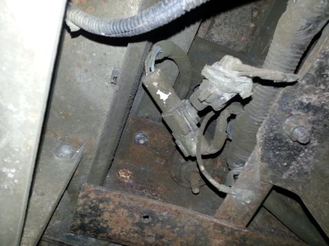 1994 Ford Bronco - Under-vehicle view of a rusty frame rail and crossmember with wiring loom, brackets, and heavy surface corrosion.