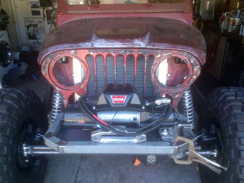 1985 Jeep CJ7 - Front view of a red Jeep CJ undergoing modifications, a Warn winch and oversized tires.
